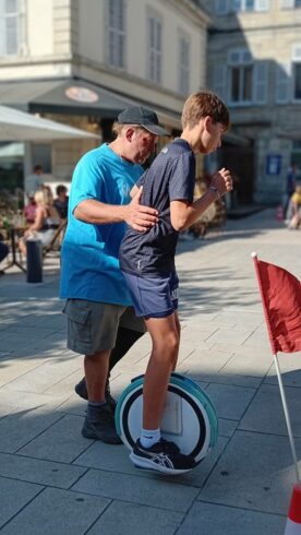Initiation en centre-ville Moniteur HelioEvents tenant un adolescent en équilibre sur une gyroroue solaire, sur une place de centre-ville