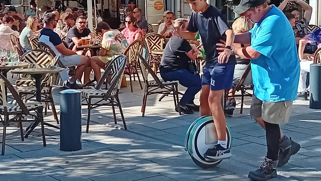 Moniteur HelioEvents guidant un jeune sur une gyroroue solaire devant une terrasse de centre-ville